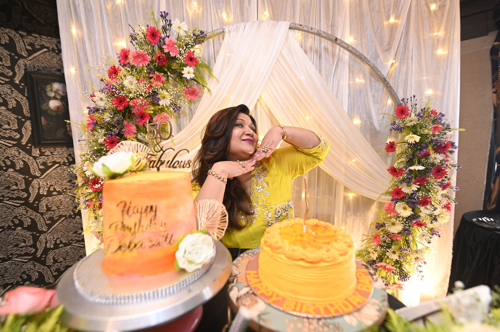 Host celebrating beside the floral backdrop