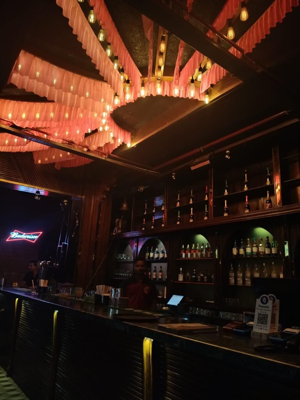 The bar floor with a sculpted pink-lit ceiling installation and a stocked back bar